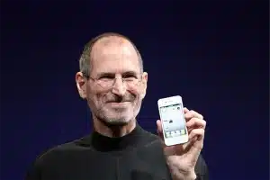 Steve Jobs segurando um smarthphone de lançamento da Apple