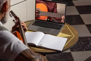 Homem tocando violão e assistindo aulas online no notebook enquanto praticava em casa treinamento online aulas online